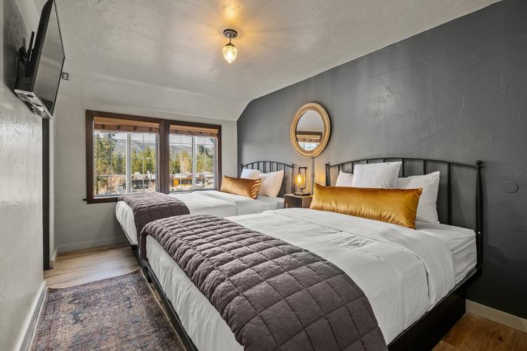 An interior shot of Sessions Retreat's "The Lodge" - there are two fluffy beds, a window, nightstand, and a television.