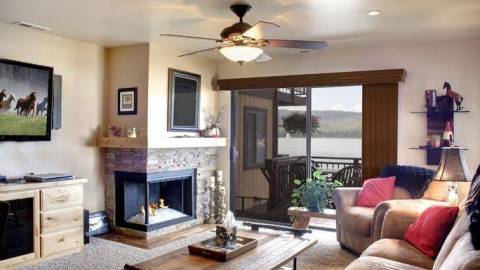 An interior shot of a cabin, there is a very modern corner styled fireplace as well as a TV and clear glass sliding doors.