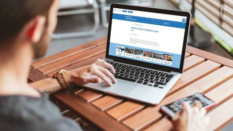 A photo of male scrolling on the BigBear.com website, he is looking at a page that states "Where To Stay."